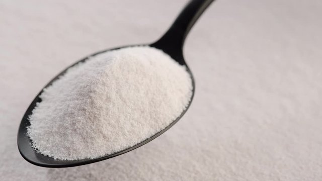 collagen powder in black spoon and collagen powder background rotating. Natural beauty and health supplement top view