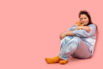 A fat sad girl sits on the floor with a bear cuddling.