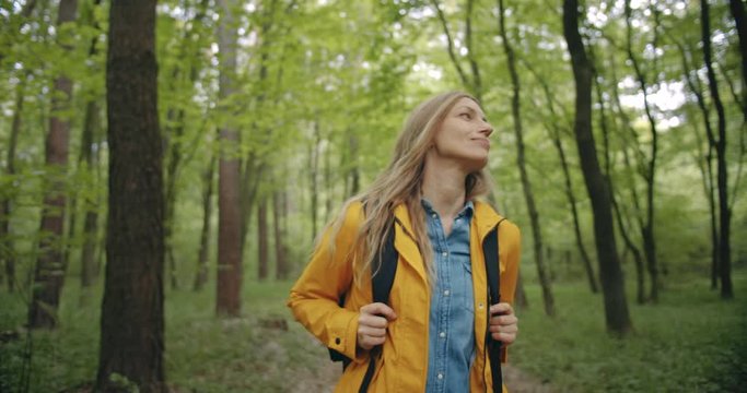 Beautiful mature woman with blond hair walking at forest with backpack. Female enjoying beautiful nature during spring time.