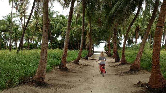 beautiful girl rides a bike around the island under palm trees, Maldives,  thoddoo island.