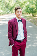The groom in a burgundy suit and the bride in a white dress with a red ribbon and a burgundy...