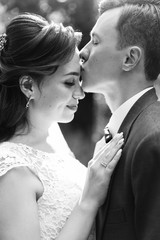 The groom in a burgundy suit and the bride in a white dress with a red ribbon and a burgundy bouquet, the newlyweds at a photoshoot, a wedding walk