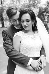 The groom in a burgundy suit and the bride in a white dress with a red ribbon and a burgundy bouquet, the newlyweds at a photoshoot, a wedding walk