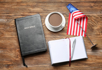 Holy Bible, notebook, cup of coffee and USA flag on wooden background
