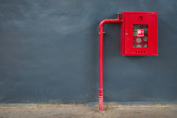 Fire hose in red box, pipe roll for fire emergency in red metal cabinet on gray painted concrete wall with tiled floor as part of firefighting system of industrial production plant with copyspace.