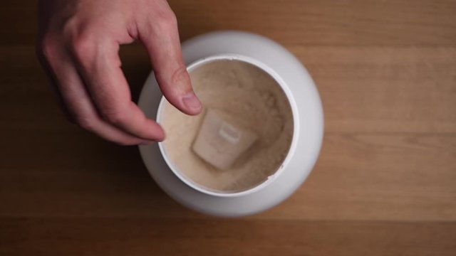 Opening jar of protein powder and taking from it with scoop. Top view