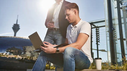 A young and an old businessman working in the city out in the sun at the notebook and have a meeting