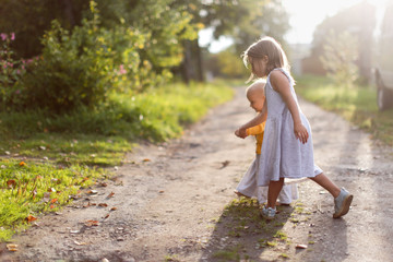 Cute Caucasian toddler kid with sister near flowers in the garden, walks with children in the park near the house and in the backyard, quarantine and stay cation