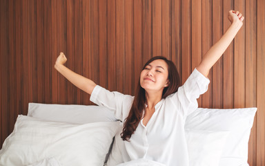 A beautiful asian woman do stretching after waking up in the morning on a white cozy bed at home