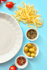 Plate with uncooked pasta and products on color background