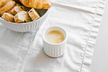 Freshly baked classic croissants and almond biscottis with cup of cappuccino on linen light background. Breakfast food concept. 
