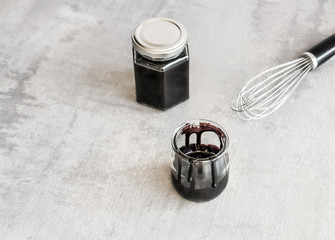 Homemade dark chocolate sauce in glass jars and silver whisk on gray background. 