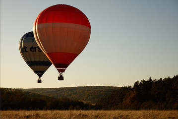 Obraz premium Group of two colorful air balloons flying over valley during summer season. Beautiful landscape and green nature. Fascinating view of air transport.