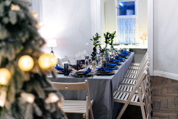Festive table professionally decorated with beautiful plates, glasses and napkins in trendy white and blue colors. Beautiful serving and decoration for christmas celebration.