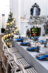 Close up of long table with porcelain crockery and shining cutlery served with green leaves and small candles. Combination of trendy blue and white colors.