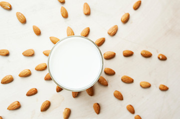 transparent mug full of milk on the background of beautifully spread almonds. Almond milk, top view
