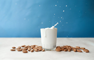splash and drops from a clear mug full of milk with beautifully arranged almonds. Almond milk on a blue background