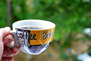 cup of coffee in hand on a background of green trees. invigorating morning coffee