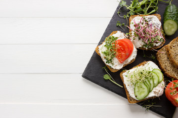 Healthy sandwiches with cream cheese , microgreens, tomatoes and cucumber on black stone board. Healthy eating, diet food, vegan food, healthy breakfast.White wooden board, empty template