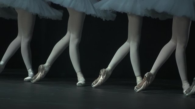 Legs view of young female ballerinas during classical performance in ballet studio spbd. Beautiful girls dancers practice in art and standing on floor in dark interior. Elegant and graceful women