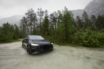 Obraz na płótnie Canvas Sporty black crossover car in water in rain on mountains background