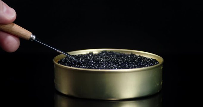Male hand with spoon is taking the caviar from tin cans.