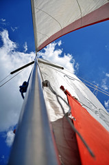 From below shot of white-red waving sail on tall mast under blue sky in clouds 