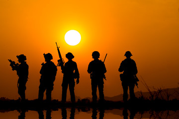 Fototapeta na wymiar The military silhouettes of soldiers hold gun against with sunset sky background.