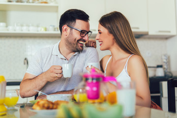 Young happy couple sitting in modern apartment and having breakfast together.