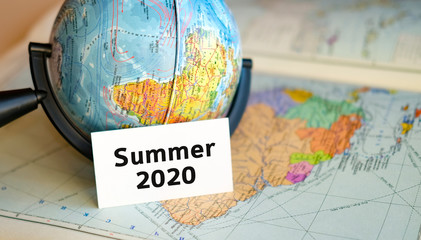 World tourism in summer 2020 - text on a white sheet in little Globe on the background of the atlas map