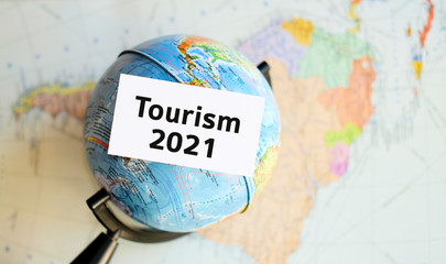 World tourism 2021 - text on a white sheet in hand against the background of the atlas map