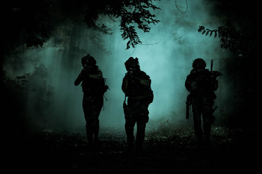 The action soldiers walking hold weapons with smoke light at night time background.