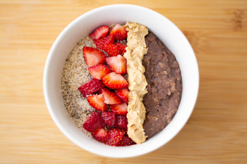 Chocolate cocoa oatmeal with almond meal, chopped strawberries and creamy peanut butter on a wooden surface. Strawberry, almonds, napkin and spoon in the background