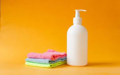 Obraz na płótnie Canvas Three colored cleaning clothes towel and white bottle for cleaning floors on yellow background.