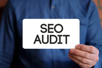 Seo audit text on a white sign in the hand of a man in a blue shirt