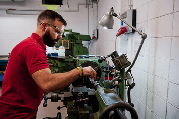 Closeup worker in uniform and protective glasses working on sharpening machine tool