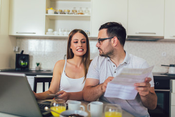 Husband and wife doing paperwork together, paying taxes online on laptop