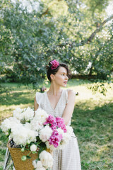 Beautiful girl on a bicycle. Girl sitting on a bicycle with flowers. Bicycle and flowers. A bunch of peonies and a girl.