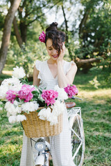 Beautiful girl on a bicycle. Girl sitting on a bicycle with flowers. Bicycle and flowers. A bunch of peonies and a girl.