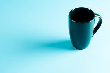 Empty a black cup of coffee isolated on cyan desk with lighting background.