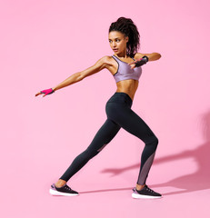 Fototapeta na wymiar Warming up before training. Photo of sporty girl with perfect body on pink background. Side view. Strength and motivation