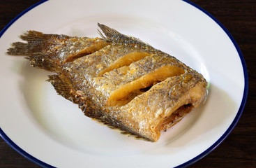 Fried crispy Gourami Fish in white dish on dark brown wooden table Thai food