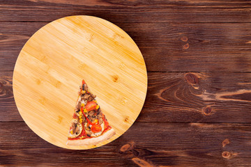 A slice of tasty pizza with mushrooms, corn, cherry tomatos, courgettes and bell peppers on a round platter which is on wooden brown background, top view and copy space