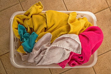 Top view of colorful towels in plastic laundry basket on tile floor.