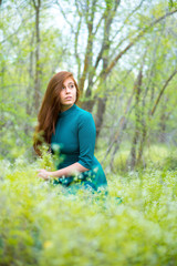 Beautiful young woman sits in green grass on blurred background.