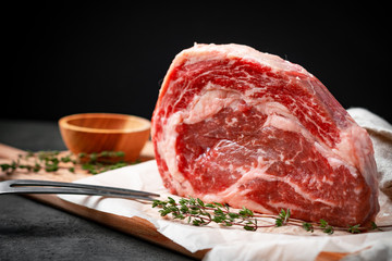 Premium raw rib eye beef steak on a wooden Board with ingredients for grilling