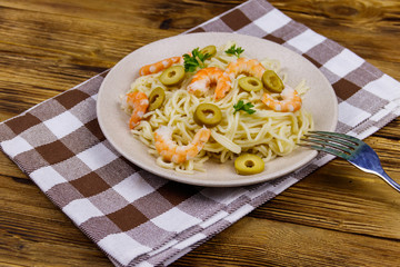 Spaghetti pasta with prawns, green olives and parsley on wooden table