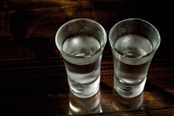 Two frozen glasses close up. Glasses with alcohol on a black wooden table. Vodka on a dark contrasting background.