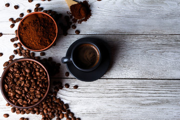 Coffee cup, scattered Arabica beans, ground coffee powder in bowl, wooden spoon on while wooden table. Top view, copy space. Coffee shop, morning, baristas workplace concept