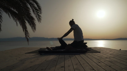 Side silhouette view of masseur doing thai yoga massage for a woman at sunrise. © Alexander Belinskiy